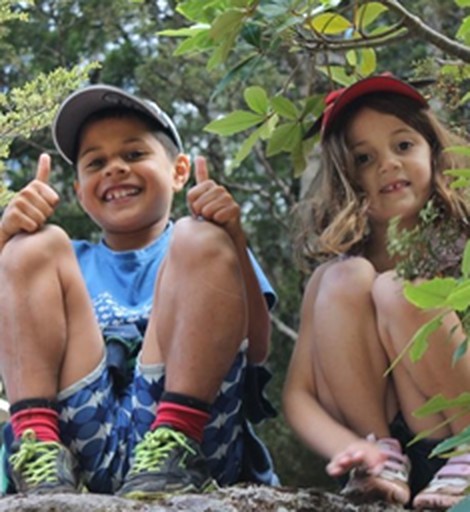 Two children smiling outdoors among trees